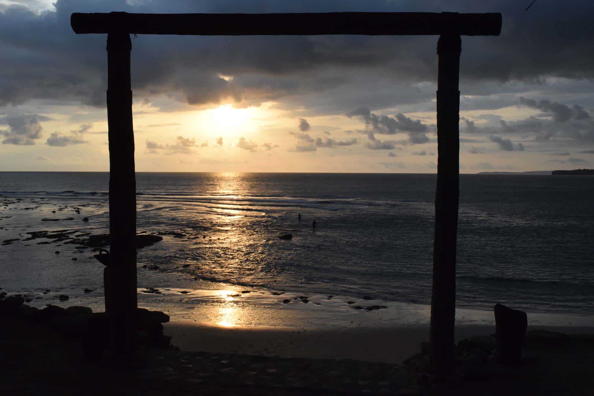 Silhouette of NIHI Coveñas’s iconic Boathouse wooden gate, overlooking Occy’s Left reef exposed during low tide at full moon, with golden sunset reflections over the ocean — capturing peace, spirituality, and the raw beauty of the island.