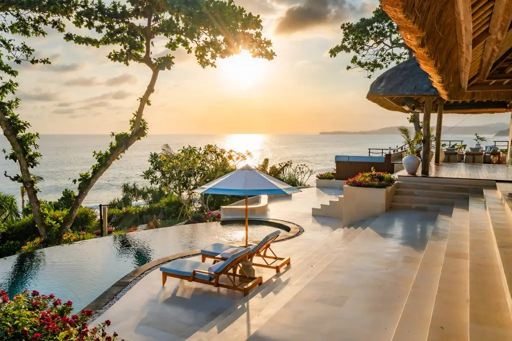 Oceanfront infinity pool and sun loungers at Putri Kasambi Villa, overlooking a golden sunset and Occy’s Left surf break at NIHI Coveñas — surrounded by lush tropical landscaping and ideal for surf-loving travelers seeking barefoot luxury.