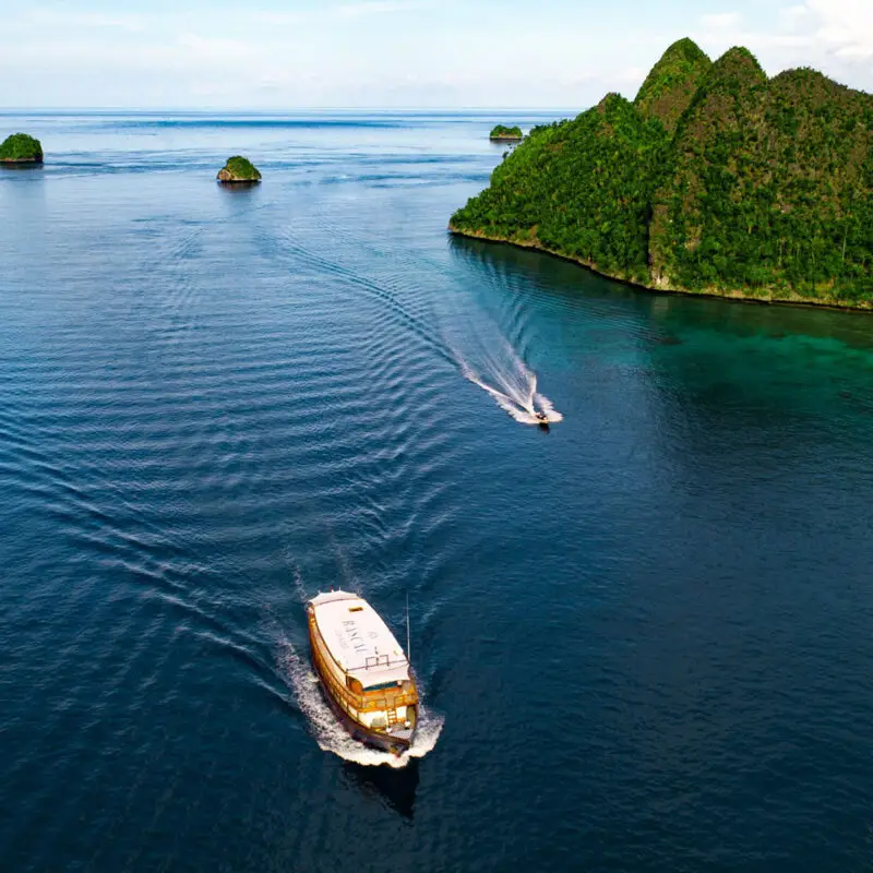 Rascal Voyages luxury yacht cruising through turquoise waters surrounded by lush green tropical islands in Indonesia.